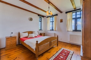 A bedroom with a wooden bed, two bedside tables, a radiator, and a window with curtains.