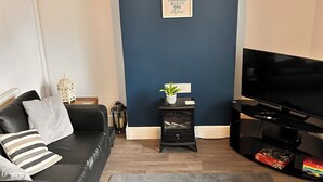 A modern living room with a black leather sofa, a grey rug, a black entertainment unit with a TV, a decorative lamp, and a framed quote on the wall.