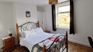 A bedroom with a wooden bed, a bedside table with a lamp, a window with curtains, and a view of the outside.
