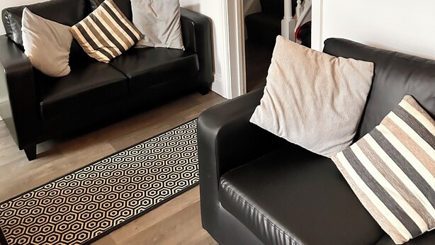 A living room with two black leather sofas, a patterned rug, and a staircase leading to a balcony.