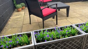 An outdoor patio with wicker furniture, red cushions, and potted plants.