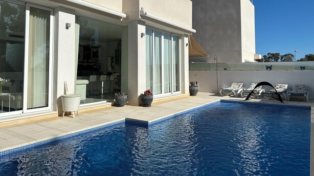 Una casa moderna con piscina, grandes puertas correderas de vidrio y mobiliario de exterior.