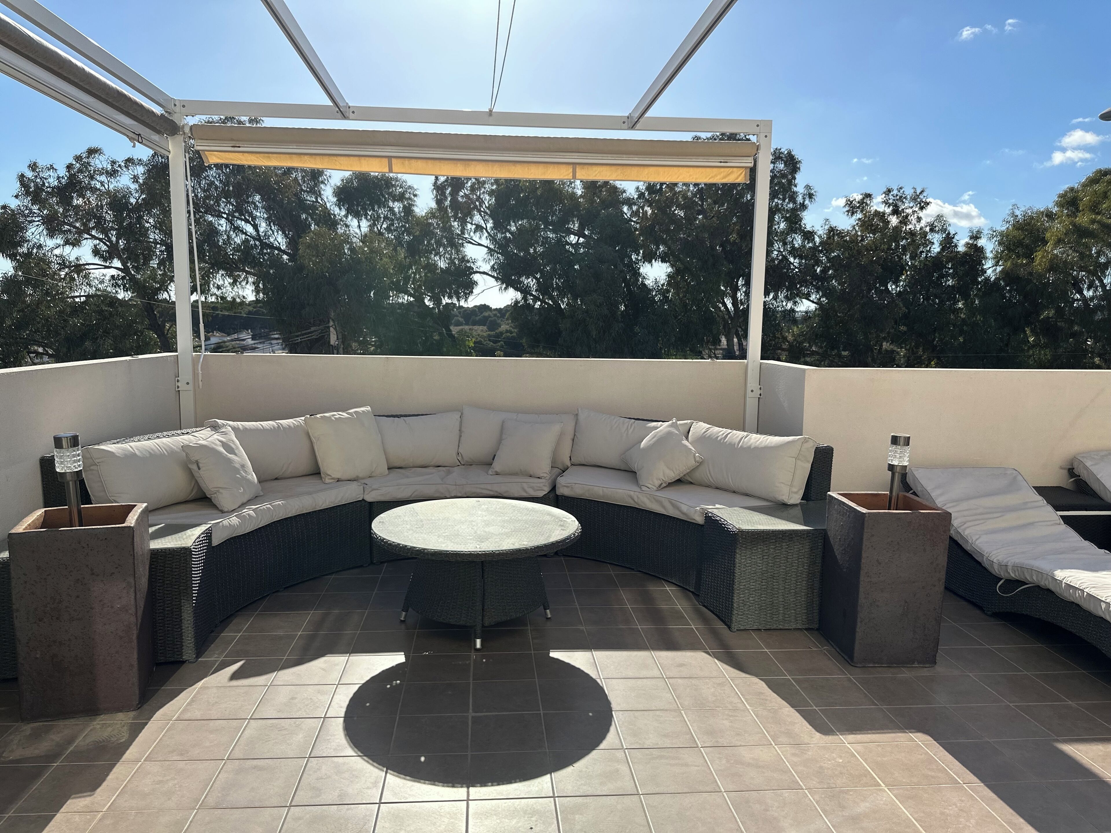 A covered outdoor seating area with a curved sofa, a round table, and two side tables.