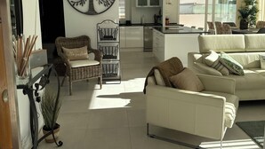 Un salón moderno con un sofá blanco, una silla de mimbre y una obra de arte de un árbol grande en la pared.