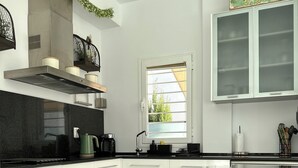 Una cocina moderna con armarios blancos, encimera negra, campana de acero inoxidable y ventana con vistas a zonas verdes.