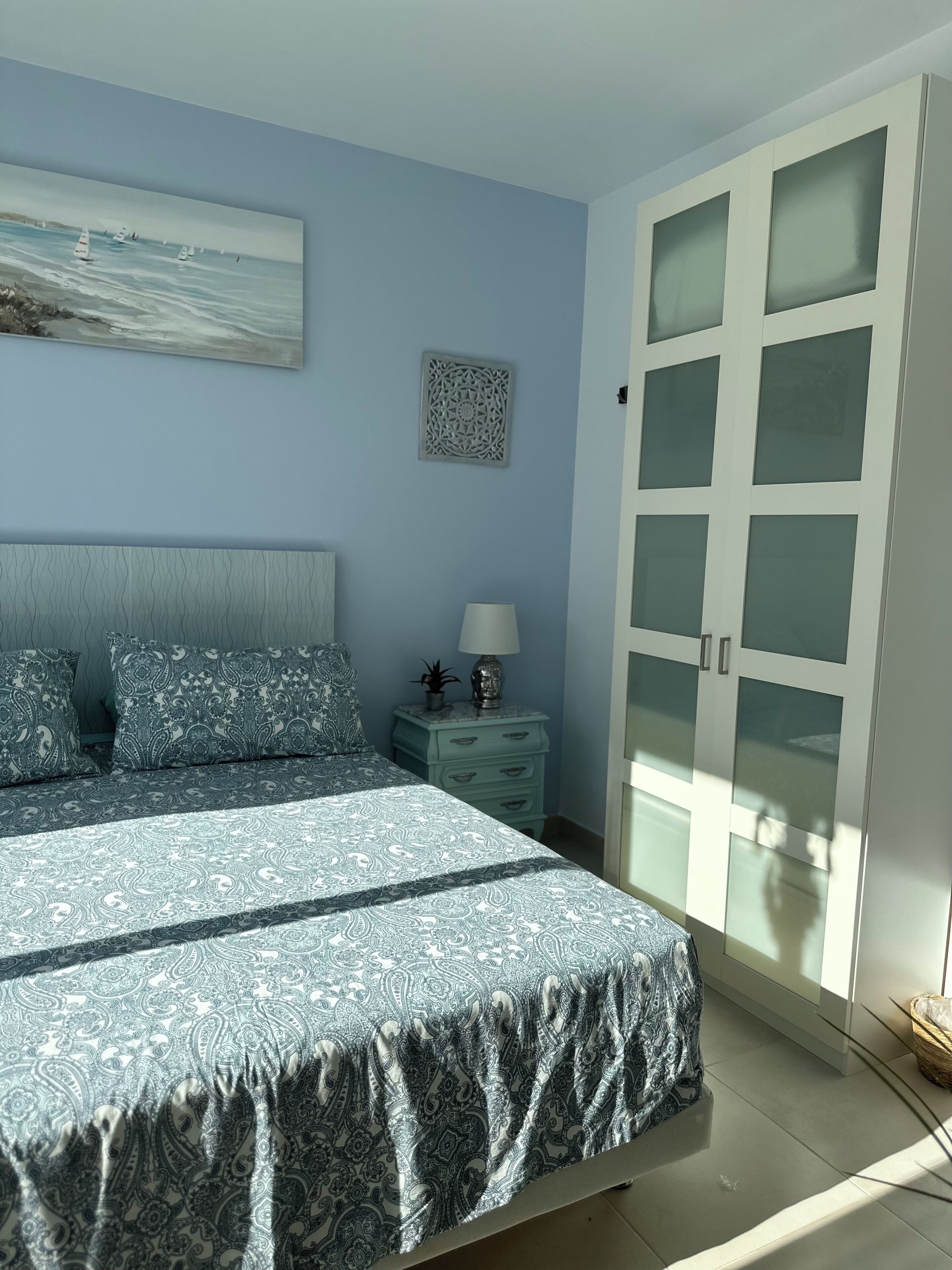 Ein Schlafzimmer mit Bett, Nachttisch, Lampe, Wanddeko und einem Kleiderschrank mit Glastüren.