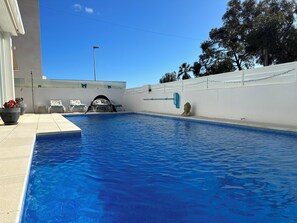Una piscina con superficie de agua azul cristalina, rodeada por un muro blanco con una estatua decorativa de Buda y una toalla azul colgada en la pared.