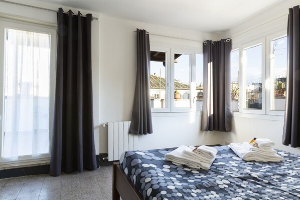 A hotel room with a bed, curtains, a radiator, and windows.
