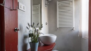 Une salle de bain avec un lavabo blanc, une plante en pot, des toilettes blanches et une douche avec des stores blancs.