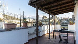 Une terrasse sur le toit, avec une table et des chaises, des plantes en pot et une vue sur le paysage urbain.