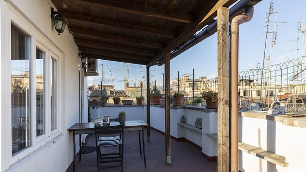 Un balcon extérieur abrité, doté d’une table et de chaises, de plantes en pot et offrant une vue sur le paysage urbain.
