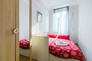 A bedroom with a bed, a window with curtains, a bedside table, and a wall-mounted light fixture.