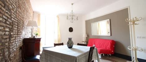 Un espace repas comprenant une table, des chaises, un lustre, un canapé rouge et un mur en briques.