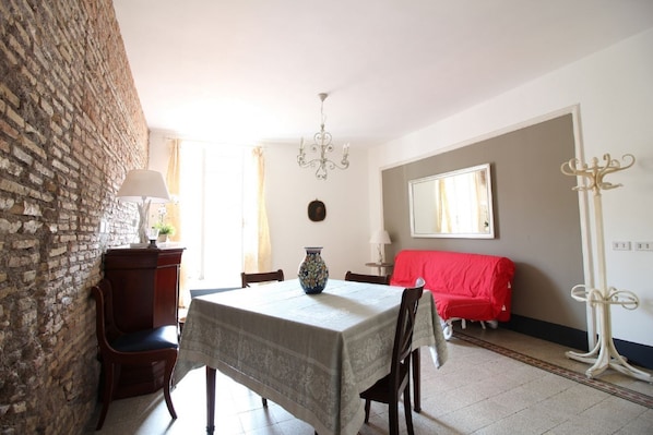Un comedor con una mesa, sillas, una araña, un sofá rojo y una pared de ladrillo.
