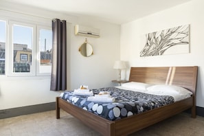 Un dormitorio con cama, un espejo redondo, aire acondicionado, una ventana con cortinas y una obra de arte en la pared.