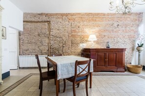 A dining area with a brick wall, wooden table, chairs, a cabinet, and a lamp. - Roof Terrace-Tetti di Piazza Navona (Roma)