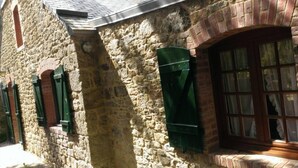 Un bâtiment en pierre, de style architectural traditionnel, avec une fenêtre dotée de volets verts et un arc en briques.