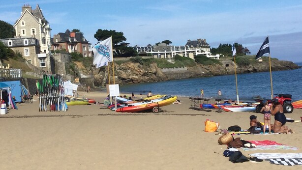 Une plage avec des kayaks, un drapeau et un bâtiment en arrière-plan.