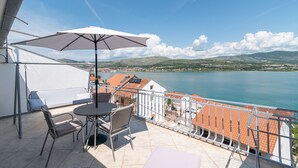 A balcony with a table and chairs, an umbrella, and a view of a lake and distant hills. - Mandic - studio apt w/ stunning sea view terrace & only 100m from the beach (Mastrinka)