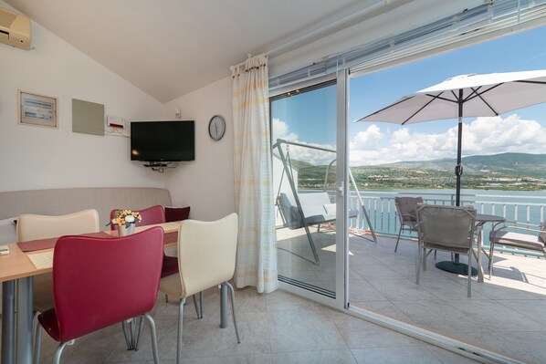 A hotel room with a balcony, a dining area with red chairs, a TV, and a view of the sea and hills. - Mandic - studio apt w/ stunning sea view terrace & only 100m from the beach (Mastrinka)