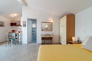 A hotel room with a bed, desk, chair, wardrobe, and a bathroom visible through an open door. - Mandic - studio apt w/ stunning sea view terrace & only 100m from the beach (Mastrinka)