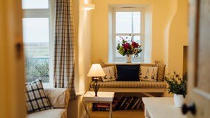 A cozy room with a sofa, a small table with a lamp, a window with a view, and a bookshelf. - Gorgeous flint cottage overlooking the marshes, walking distance to beach (Nr Cley next the Sea)
