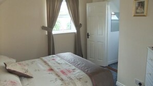 Un dormitorio con cama, ventana con cortinas, puerta y cómoda.
