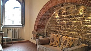A cozy room with a stone wall, a cushioned bench, and a window with a view of buildings. - King Suite - Michelangelo (Arezzo)