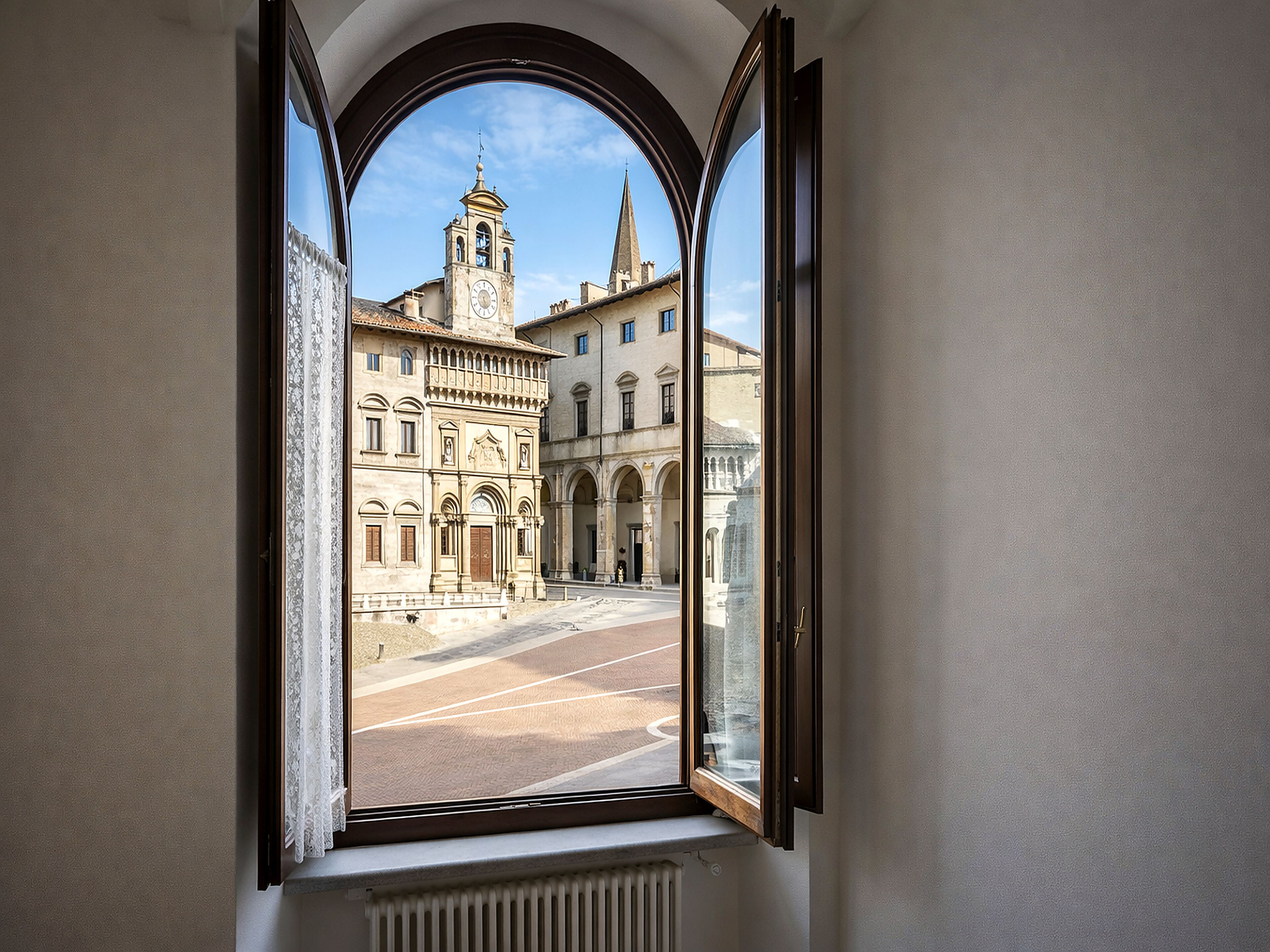 Una finestra che offre una veduta ad arco su un edificio con una torre dell'orologio e una guglia di chiesa.