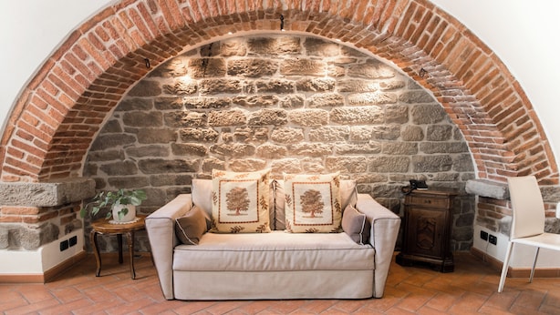 A cozy seating area with a stone fireplace, a cushioned sofa, and a small table with a plant. - King Suite - Michelangelo (Arezzo)