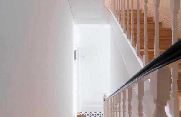 Un escalier avec des balustrades blanches et une main courante en bois menant à une pièce dont le sol est recouvert de carreaux.