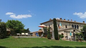 A historic stone building with a tiled roof, a flag, and outdoor seating. - Beautiful rustic villa in Tuscany in Monteriggioni, between Siena and Florence.  (Monteriggioni SIENA)