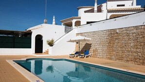 Una piscina con lettini e una parete in pietra.