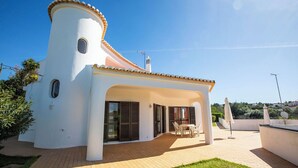 Una villa moderna con una facciata bianca curva, un tetto in tegole e una zona patio con mobili da esterno.
