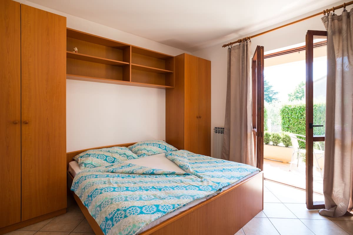 Une chambre avec un lit, une armoire en bois et une porte-fenêtre coulissante donnant sur un espace extérieur.