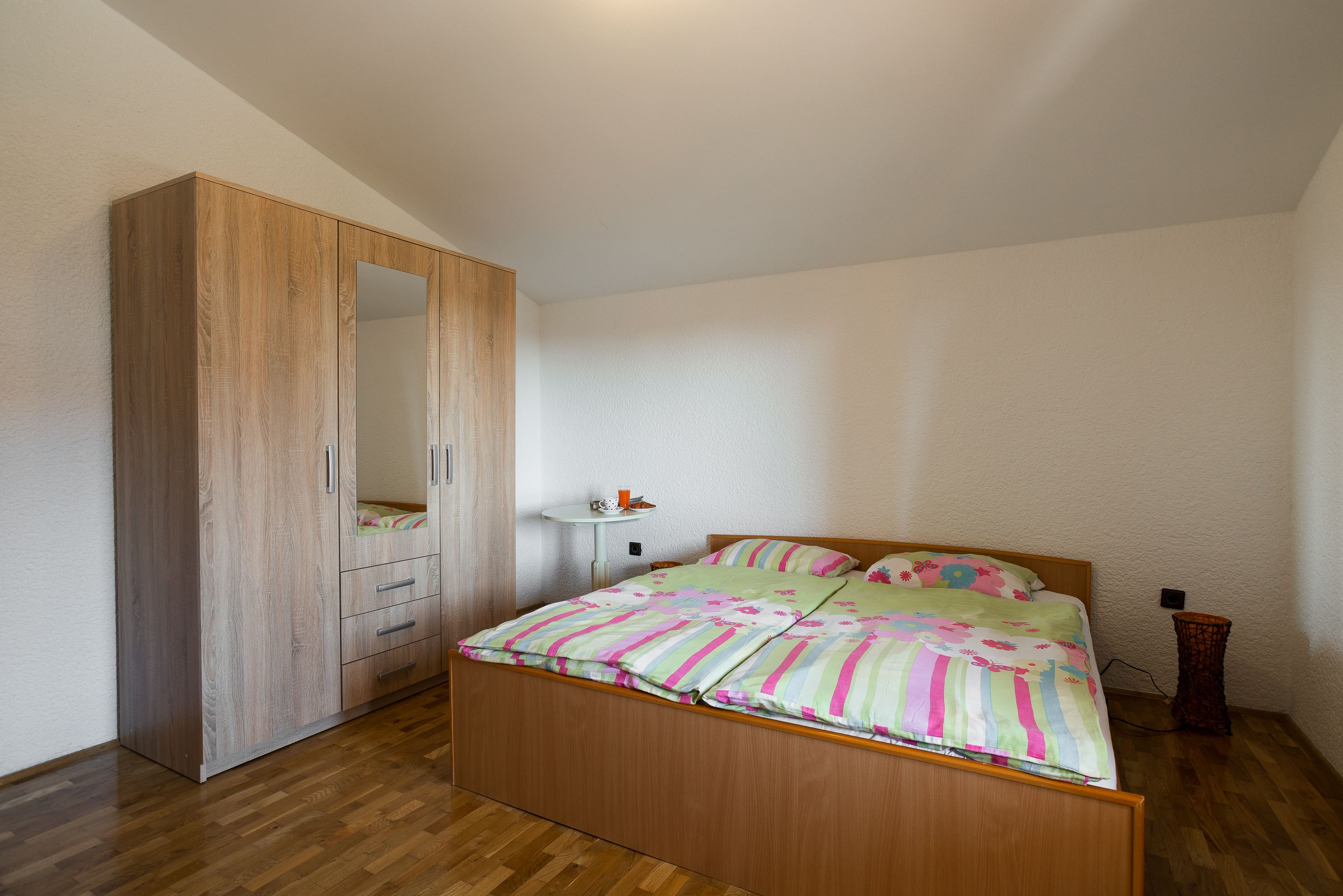 Une chambre avec une armoire en bois, un lit avec une literie à rayures et une table de chevet avec une lampe.