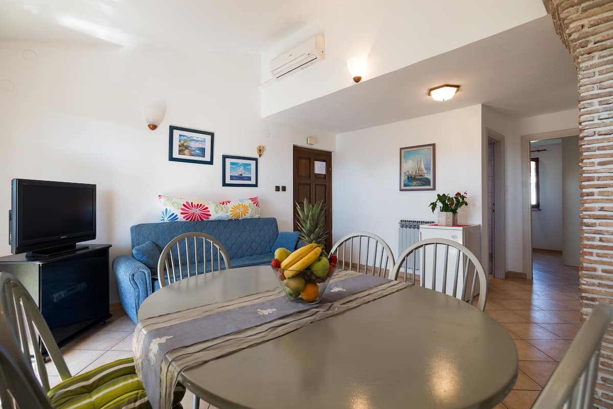 Un coin repas avec une table dressée pour quatre personnes, un téléviseur et un canapé bleu.