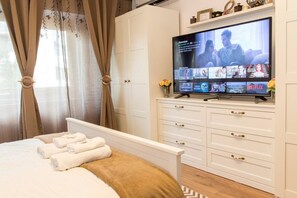 Habitación de hotel con cama, televisor mostrando una película, armario y ventana con cortinas.