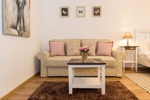 Una habitación acogedora con un sofá color beige, una mesita blanca con un florero y una lámpara en una mesita de noche.