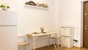 A compact kitchen with a white refrigerator, a small cabinet, a white desk with two chairs, and a shelf above the desk with decorative items. - Motru 75 by MRG Apartments | Chic & Spacious Retreat in Central Area (București)