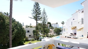 En balkon med pool, omgivet af hvide bygninger og grønt.