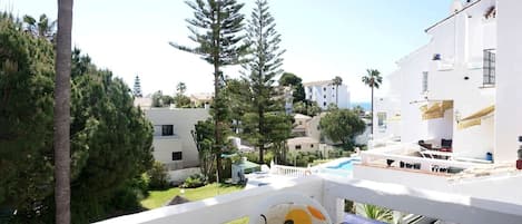 A balcony with a pool, surrounded by white buildings and greenery.