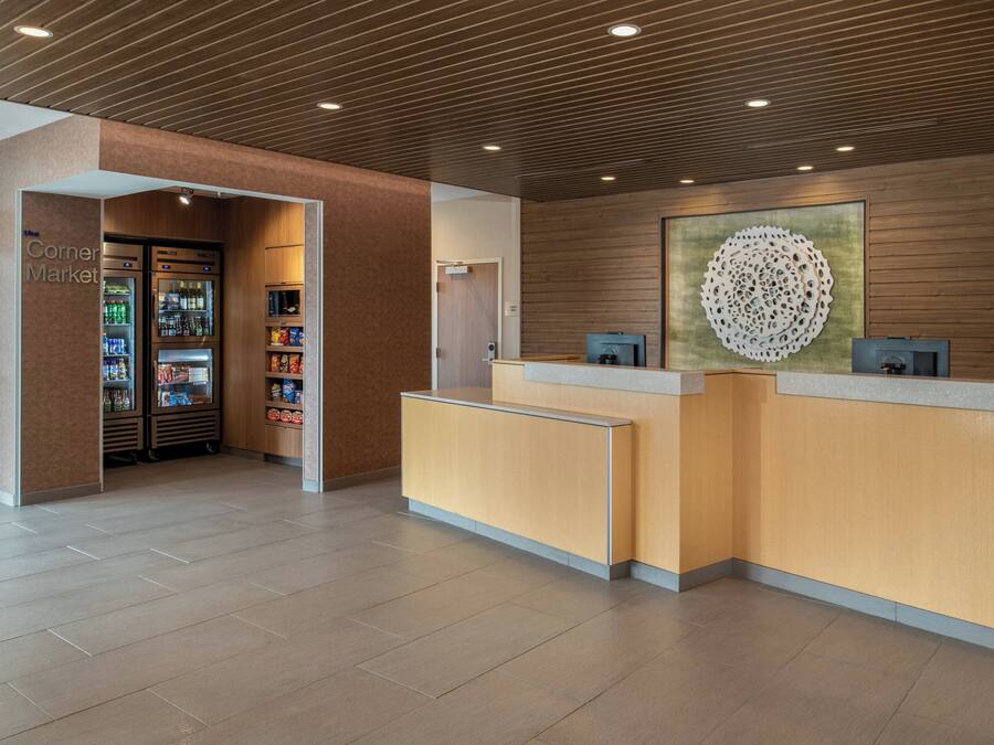 A reception area with a wooden reception desk, a corner market with refrigerated drinks, and a decorative wall piece.