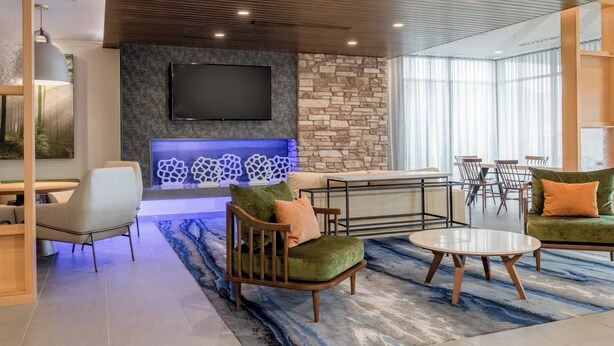 Una sala de estar moderna con una pared de acento de piedra, un televisor de pantalla plana y un área de descanso con un tapete azul estampado.