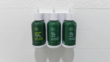 Three bottles of body wash, conditioner, and shampoo on a white tiled wall.