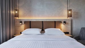 A modern hotel room with a large bed, two wall-mounted lamps, and a view of the sky through the window. - Moxy Frankfurt Airport Kelsterbach (Kelsterbach)