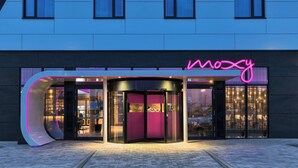 A modern building with a curved entrance and a neon sign that reads "moxy". - Moxy Frankfurt Airport Kelsterbach (Kelsterbach)