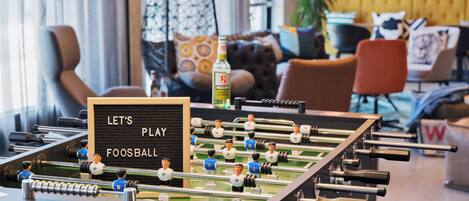A foosball table in a modern lounge area with a sign that reads "LET'S PLAY FOOSBALL".