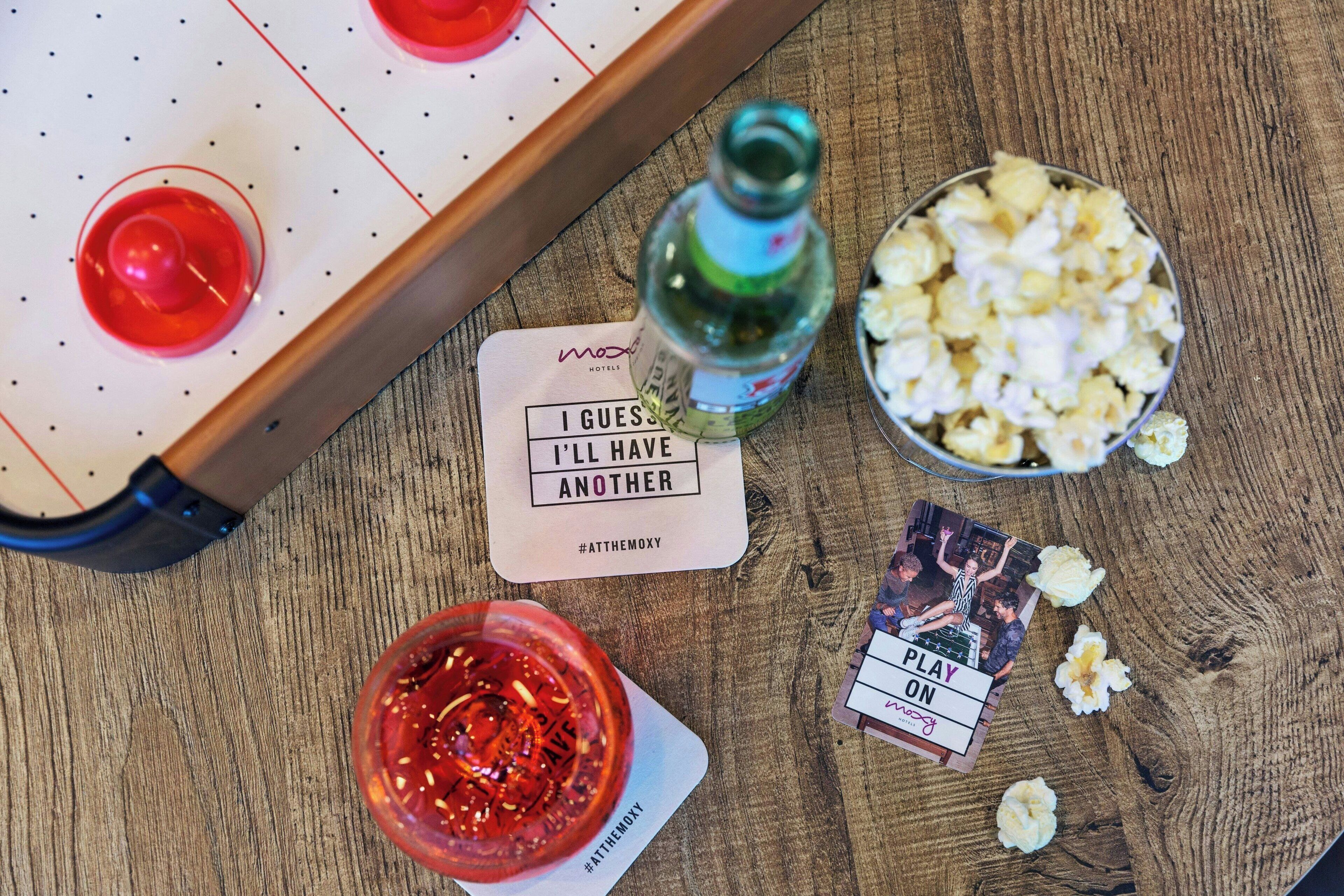 Une table en bois, un baby-foot, une bouteille de liqueur, un bol de pop-corn et un jeu de cartes.