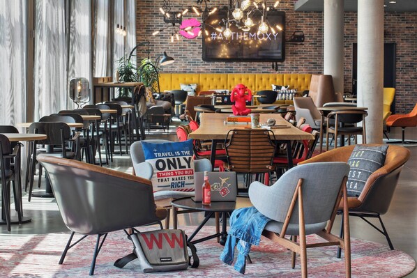 A modern dining area with multiple tables and chairs, a yellow cushioned bench, and a red statue. - Moxy Frankfurt Airport Kelsterbach (Kelsterbach)